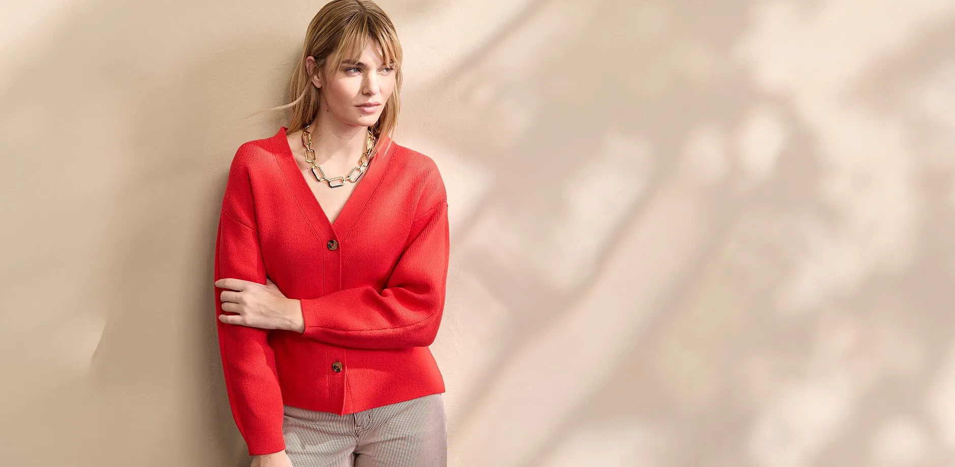 Un cardigan rosso brillante con scollo a V e bottoni, abbinato a una vistosa collana dorata.