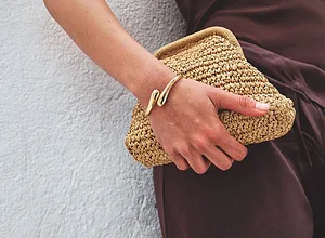 Elegante abito marrone abbinato a una clutch in paglia estiva. Bracciale dorato come tocco di stile. 