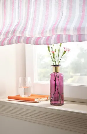 Tenda a pacchetto a righe in tonalità pastello adorna la finestra, con un vaso rosa pieno di fiori. 