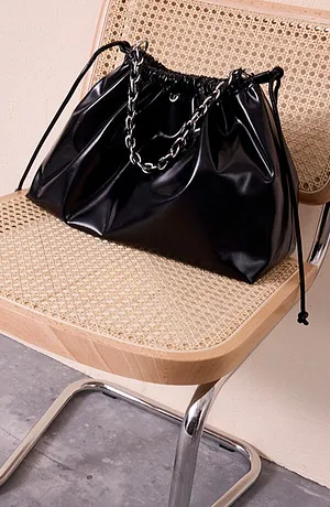 Borsa nera lucida con manico a catena su una sedia di legno. 