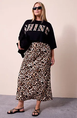 Donna con maglia corta nera con scritta SHINE leopardata, gonna lunga leopardata, occhiali da sole neri e borsa nera lucida.