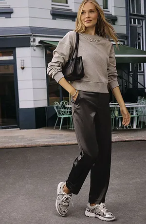 Stile streetwear casual: maglione beige, pantaloni scuri e sneakers bianche. Borsa nera come accessorio.