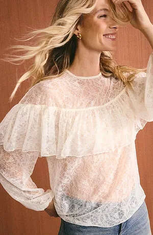 Camicetta leggera in pizzo con volant e maniche lunghe, abbinata a jeans casual per un look femminile.