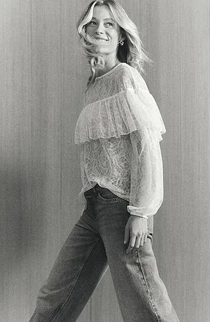 Romantica camicetta bianca in pizzo con volant, abbinata a jeans classici per un look casual-elegante.