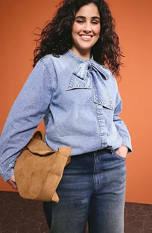 Camicia di jeans azzurra con colletto a fiocco, jeans scuri e borsa in pelle marrone per un look casual di tutti i giorni.
