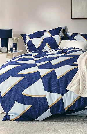 Biancheria da letto in fantasia geometrica in blu e bianco, completata da una coperta color crema.