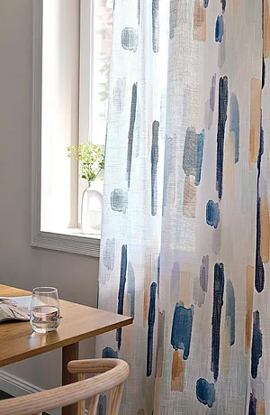Tende leggere con pennellate blu-grigie decorano la finestra e lasciano entrare una luce soffusa.