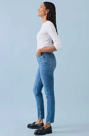 Look casual con maglia bianca a maniche lunghe, jeans blu aderenti e scarpe di pelle nere.