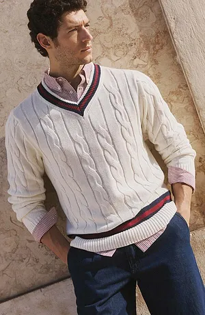 Maglione bianco con motivo a trecce, abbinato a jeans e camicia a quadretti bianca e rossa.