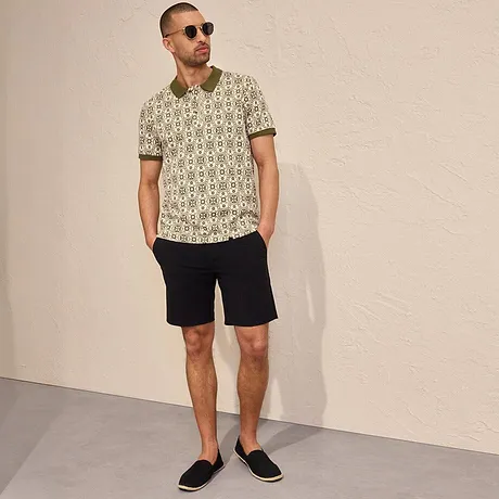 Polo a fantasia e pantaloncini scuri per un look estivo casual, completato da occhiali da sole ed espadrillas. 