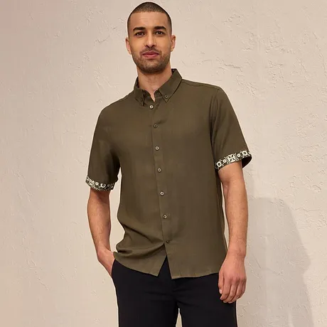 Camicia a maniche corte verde oliva con risvolto a fantasia, pantaloncini scuri ed espadrillas nere.