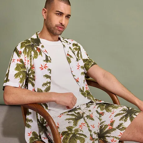 Completo due pezzi: camicia a maniche corte tropicale e shorts con motivo di palme. Sotto una semplice t-shirt bianca.