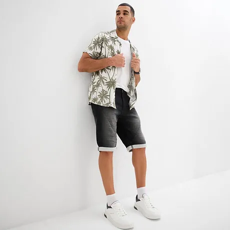 Camicia hawaiana estiva con motivo di palme, T-shirt bianca, pantaloncini di jeans grigi e sneakers bianche. 