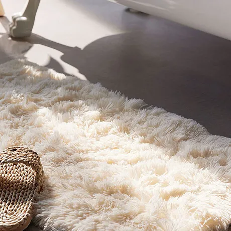 Tappeto bianco soffice a pelo alto per il bagno, con sopra ciabatte estive in corda intrecciata.