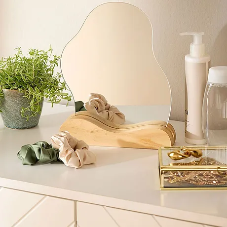 Comodità e leggerezza estiva in un'immagine. Fascia per capelli beige e elastici su superficie chiara accanto a uno specchio, pianta e prodotti di bellezza. 