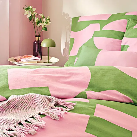 Biancheria da letto fresca in rosa e verde, decorata con motivi geometrici. Una coperta intrecciata completa il look. 