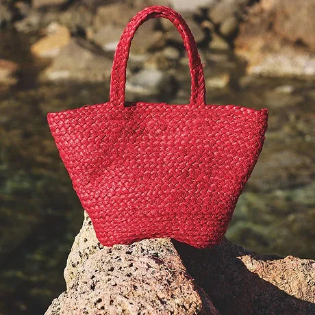Borsa di paglia rossa brillante appoggiata in bella vista sugli scogli, perfetta per una giornata in spiaggia.