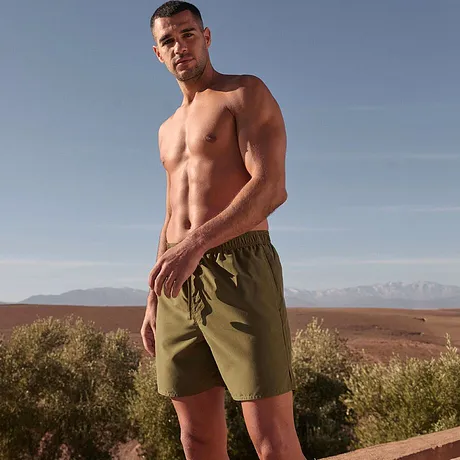 Costume da bagno a pantaloncino verde oliva che esalta il fisico atletico.