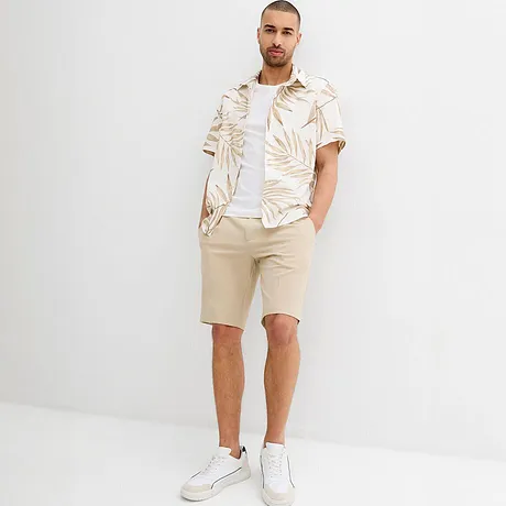 Outfit estivo con pantaloncini beige e camicia bianca con motivo tropicale.