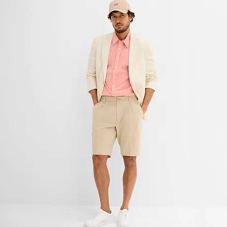 Elegante blazer color crema con camicia rosa, sneaker bianche e berretto beige. 