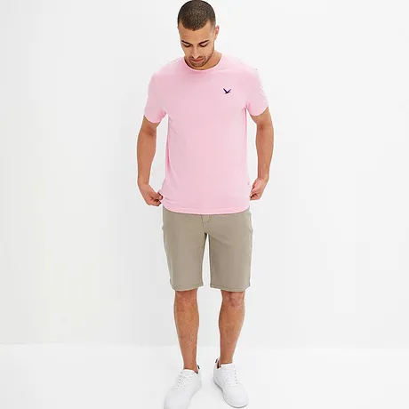 Una maglietta rosa con un piccolo logo e pantaloncini beige creano un outfit estivo. 