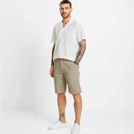Camicia bianca a maniche corte con motivo, pantaloncini beige e sneaker bianche.