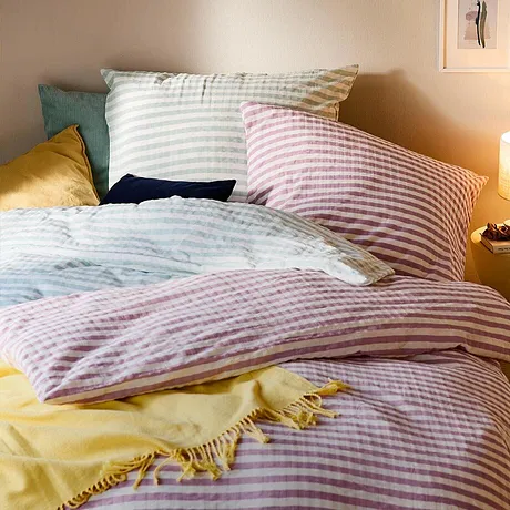 Biancheria da letto a righe in tonalità pastello decora il letto accogliente. Una coperta gialla aggiunge un tocco di colore. 