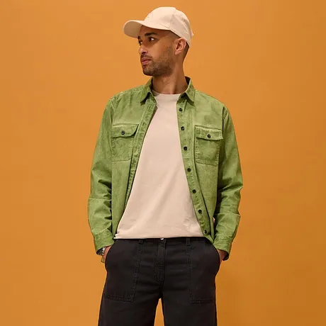 Camicia verde sopra una maglietta bianca, pantaloncini scuri, sneakers bianche e cappellino da baseball. 