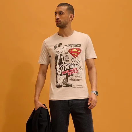 T-shirt bianca con stampa di Superman, pantaloncini scuri e sandali.
