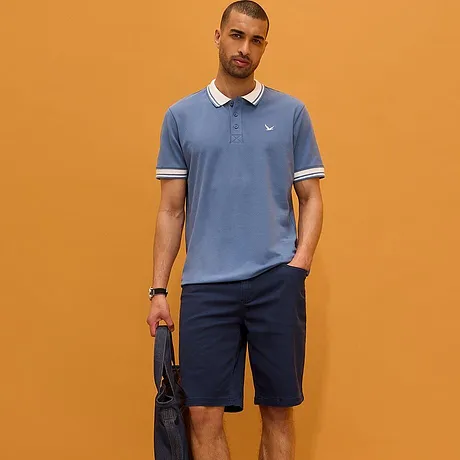 Polo azzurra con colletto bianco e bermuda scuri. Look sportivo-elegante per il quotidiano.