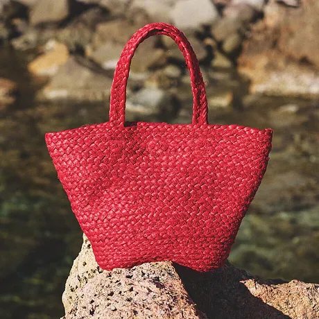 Borsa in paglia rossa poggiata sugli scogli, perfetta per una passeggiata in spiaggia.