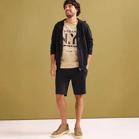 Look casual con t-shirt beige, felpa con cappuccio nera e pantaloncini felpati scuri.