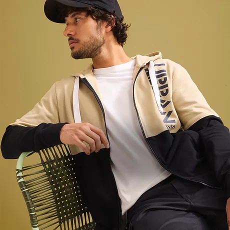 Look urban: giacca beige, t-shirt bianca, pantaloni scuri e berretto.