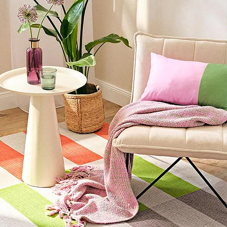 Tessuti color pastello in rosa e verde decorano l'area salotto con coperta e cuscini. 