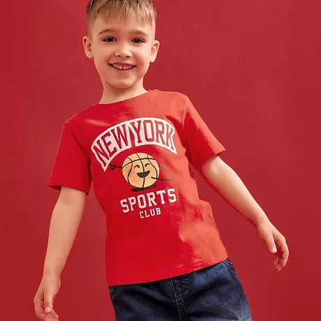 T-shirt rossa con scritta "New York Sports Club", abbinata a jeans blu.
