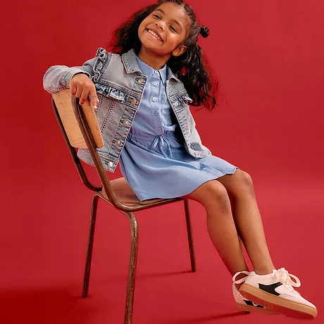 Bimba allegra in abito azzurro e giacca di jeans, con comode sneaker.