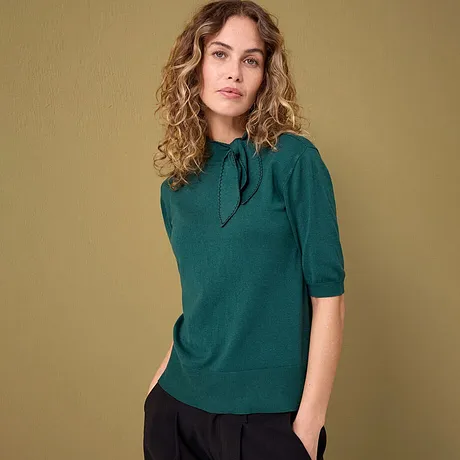 Un elegante maglione color smeraldo a maniche corte, abbinato a pantaloni scuri.