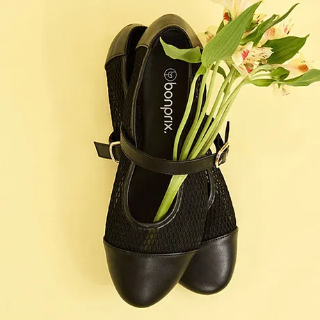 Scarpe da donna nera con cinturino e tessuto a rete, riempite di fiori freschi.