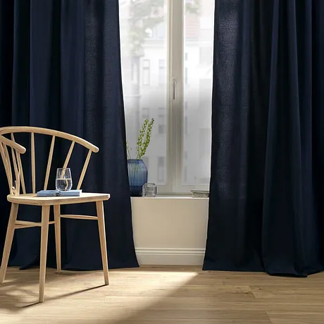 Tende blu scuro incorniciano la finestra luminosa, mentre una sedia color legno si trova accanto.