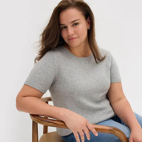 Maglione grigio a maniche corte abbinato a jeans blu.