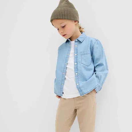 Camicia di jeans azzurra sopra una maglietta bianca, pantaloni beige e berretto di maglia verde: look casual per bambini.