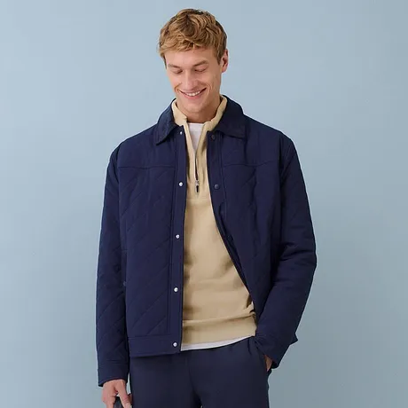 Giacca trapuntata blu scuro abbinata a un maglione beige e pantaloni blu.