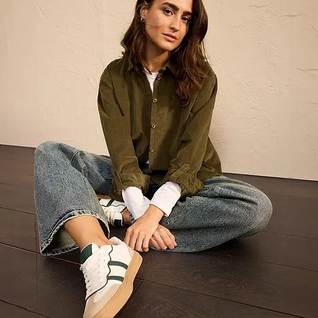 Giacca verde oliva con jeans e sneakers bianche con strisce verdi.