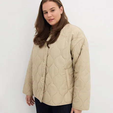  Giacca trapuntata beige con bottoni, abbinata a pantaloni scuri. 