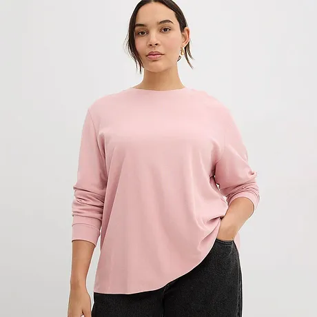 Una maglia a maniche lunghe rosa tenue con scollo rotondo completa perfettamente i pantaloni scuri.
