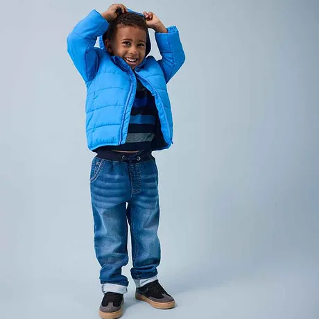 Giacca imbottita blu, maglietta a righe e jeans: moda infantile allegra per le giornate fredde. 