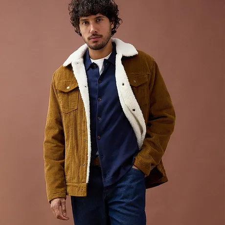 Giacca di velluto a coste marrone con collo di montone sopra un maglione blu.