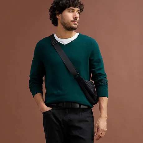 Elegante maglione verde scuro sopra una maglietta bianca, abbinato a pantaloni neri.
