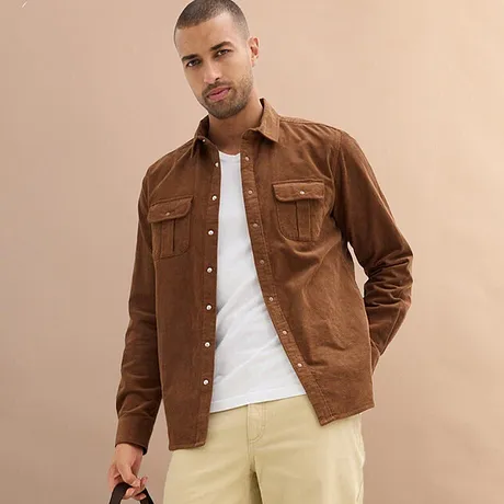 Camicia marrone sopra una maglietta bianca, abbinata a pantaloni chiari.