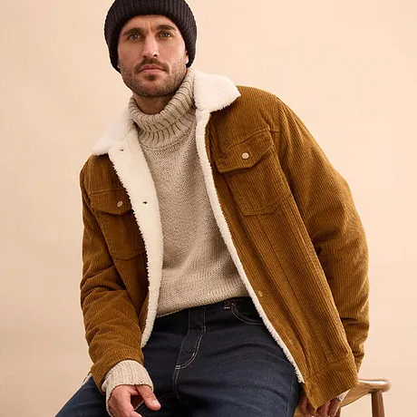 Maglione beige lavorato a maglia, giacca marrone in velluto a coste con collo di pelliccia e jeans scuri.